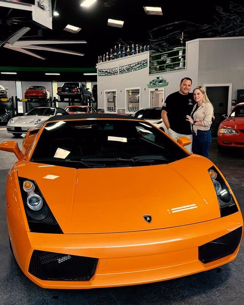 Steven Stebbins and a companion beside an orange 2008 Lamborghini Gallardo in the showroom
